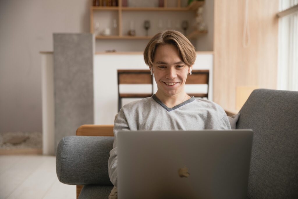 Smiling young man using a laptop on a couch at home, symbolizing remote work and digital lifestyle.