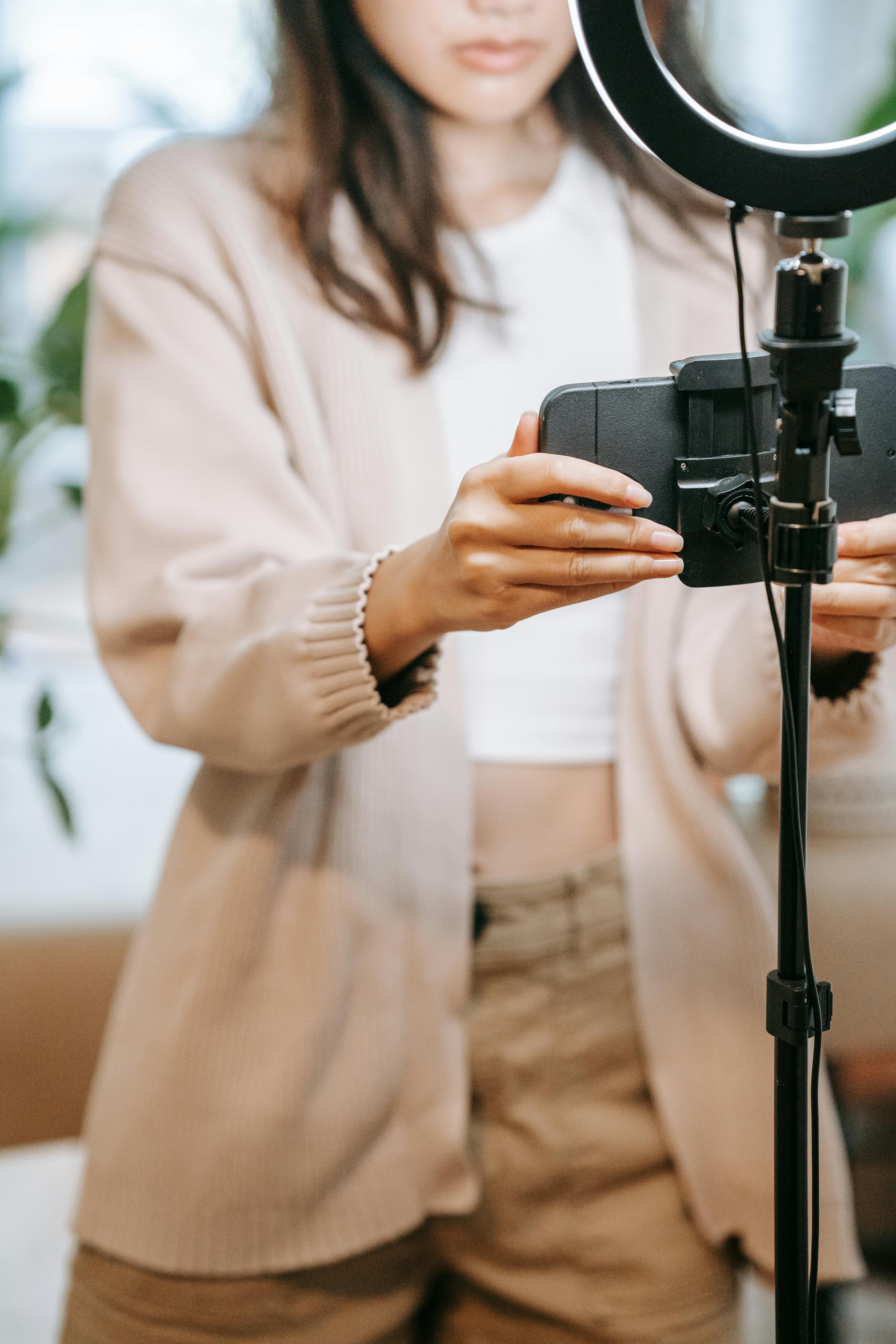 Young woman adjusting smartphone and ring light equipment for indoor vlogging setup.